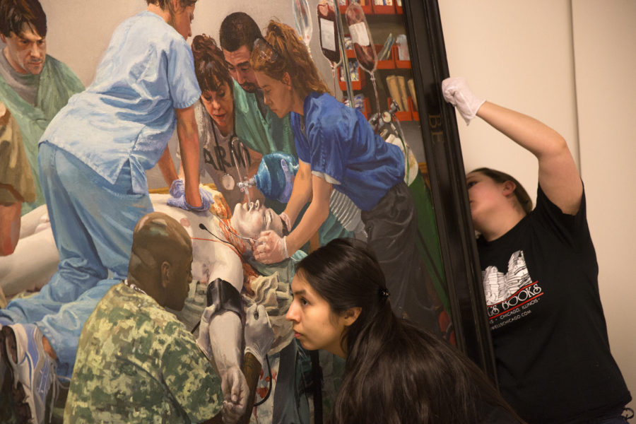 Monse Wisdom, left, and Destinee Oitzinger hang a painting titled We Could be Heroes by artist Steve Mumford for the Joe Bonham Project, a collection of drawings and paintings of severely injured soldiers in VA hospitals, at the National Veterans Art Museum in Chicago on Thursday, May 21, 2015. (Source: Tribune News Service)