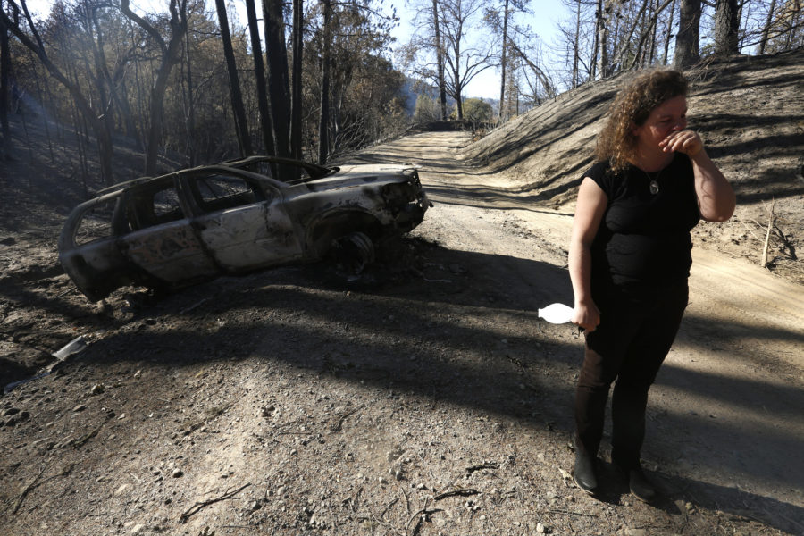 An emotional Charlotte Scott stands near her charred Volvo in Redwood Valley, Calif., on October 18, 2017. On the night of the Redwood Valley fire, Scott raced her car down the roughly three-mile dirt road from her house with her two daughters, 3 and 7, and her 9-year-old stepson and 14-year-old stepdaughter. She reversed to do a three-point-turn on the narrow road with almost no visibility. She misjudged, and her back wheels dropped into a ditch. (Genaro Molina/Los Angeles Times/TNS)