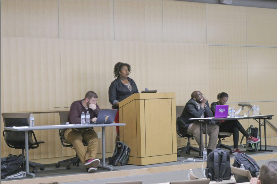 Zach Baker (left), Terri Hughes (podium), Jean-Michel Habineza (center), and Loanes Rwiranzira (right) at the Rwanda Debate. (Sarah Catan / The Signpost)