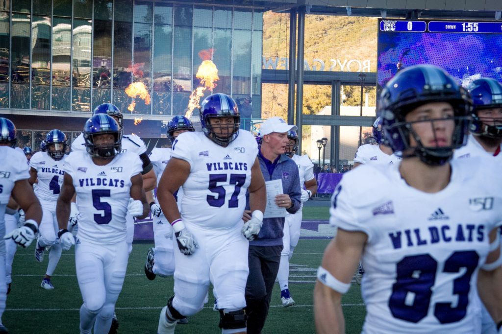 The Weber State Wildcat football team runs onto the field before the game begins while pyrotechnics erupt in the background. (Kalie Pead/ The Signpost)