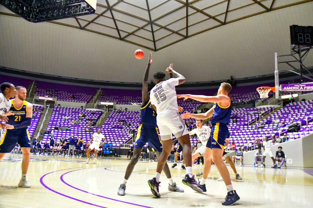 Weber State's David Nzekwesi passes the ball despite the defense by Northern Arizona, contributing to another two points, in Thursday's game.  (Nikki Dorber / The Signpost)