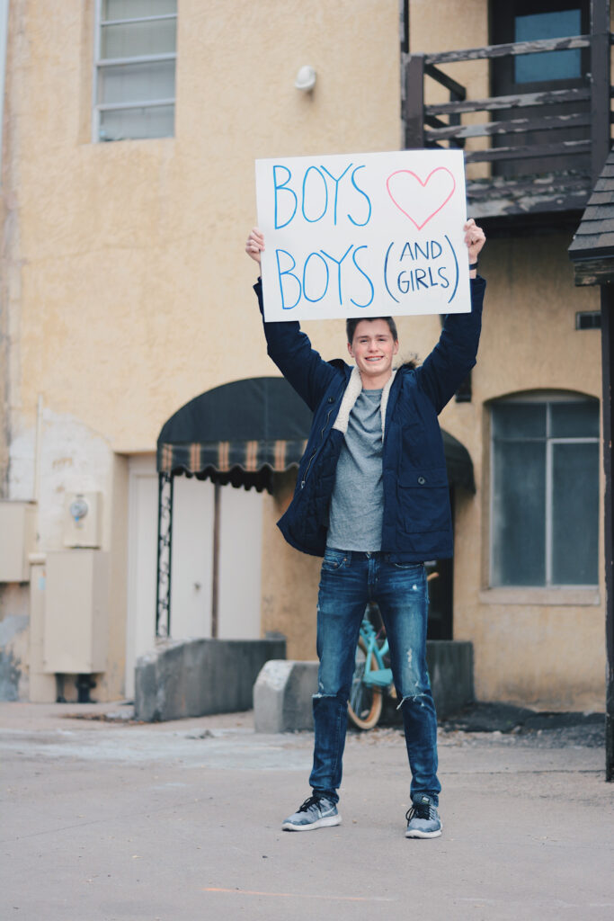 Braeden Budge holds up a poster that reads "BOYS ♡ BOYS (AND GIRLS)," Sunday, Mar. 14, 2021, in Logan, Utah. (Brooklynn Kilgore/ The Signpost)