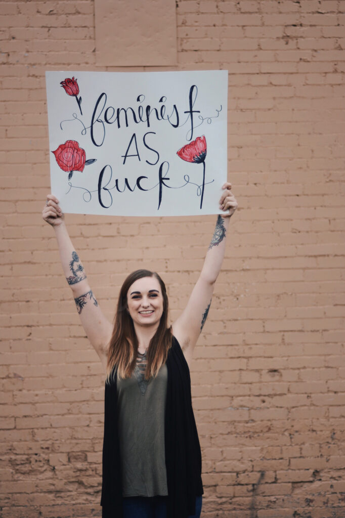 Mellory Barnes raises a sign reading "feminist as fuck," Sunday, Mar. 14, 2021, in Ogden, Utah. (Brooklynn Kilgore/The Signpost)