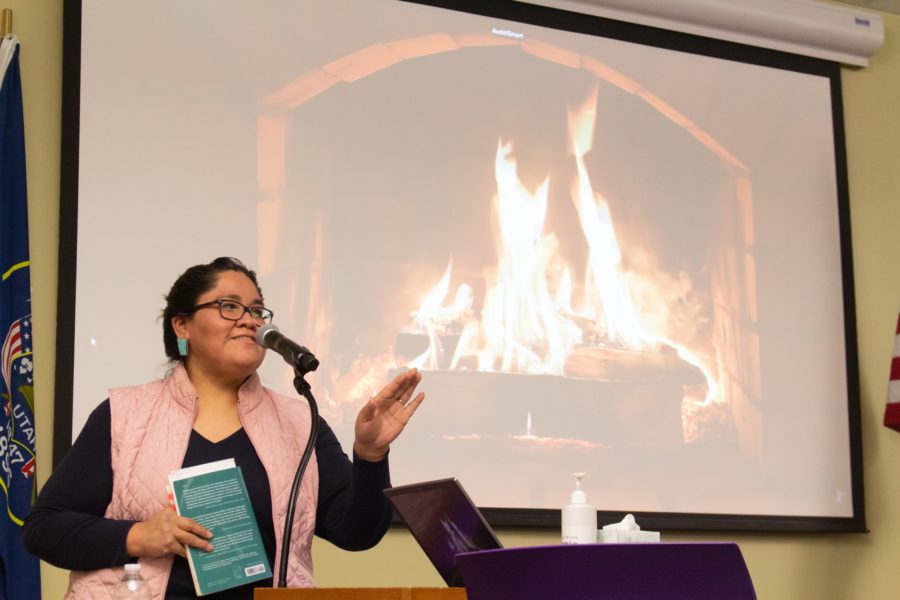 Tracey M. Atsitty reading out of her book Rain Scald in front of a projection of a crackling fire. The fire was specifically chosen for poetry night to create a calm environment and bring life to the poetry read that night. (Kennedy Robins/ The Signpost) Photo credit: Kennedy Robins