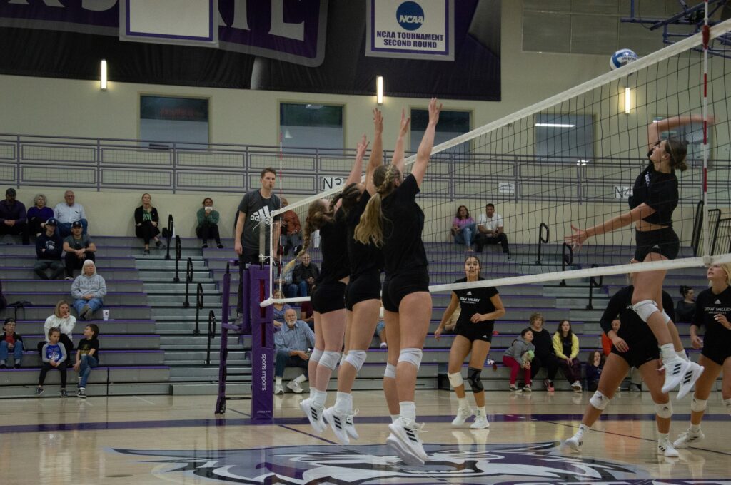 Three Weber State volleyball players jump to block a spike from a UVU player. (Summer Muster/The Signpost)