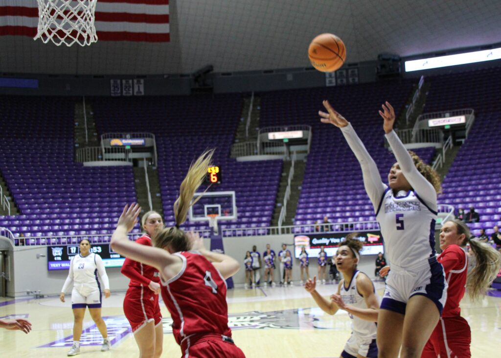 Jadyn Matthews extends her arms mid-jump shot while her teammates prepare to attempt getting a rebound. (Summer Muster/The Signpost)