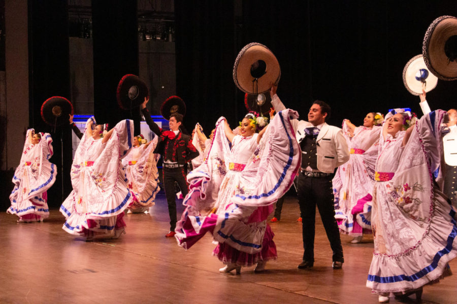 The Ballet Folklórico dancers smile at their audience while raising their dresses and hats in the air.