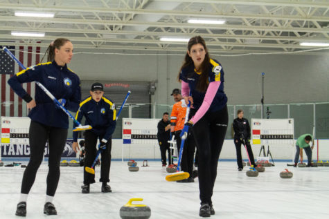 Anastasiia Kotova, Nikolov Eduard and Yaroslava Kalinichenko preparing to sweep the ice in front of a granit stone.