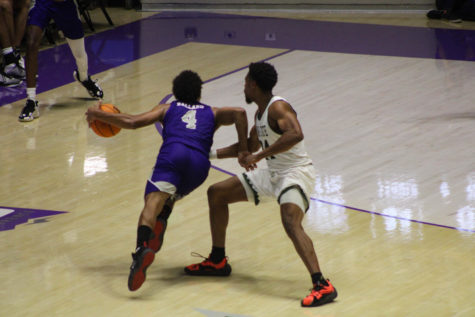 Guard position Junior Ballard running past Adams State player Sterling Benjamin, while dribbling the ball towards the basket.