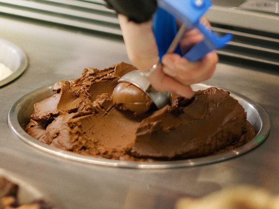 A person scooping chocolate ice cream with an ice cream scoop.