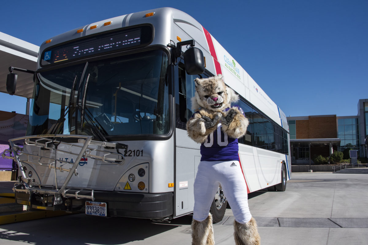 Waldo the Wildcat posing in front of the OGX bus, while forming a W with his paws.