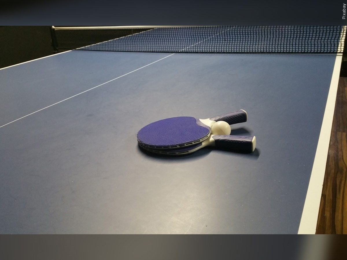 Table Tennis paddles lay flat on a table alongside a ping pong ball next to the net.
