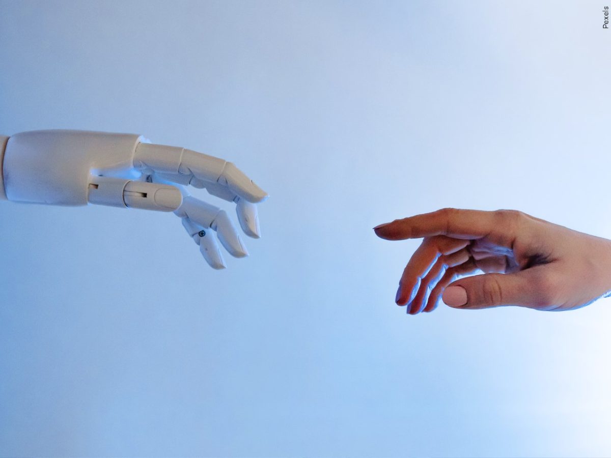 A photo of a robot hand and human hand reaching out towards each other.