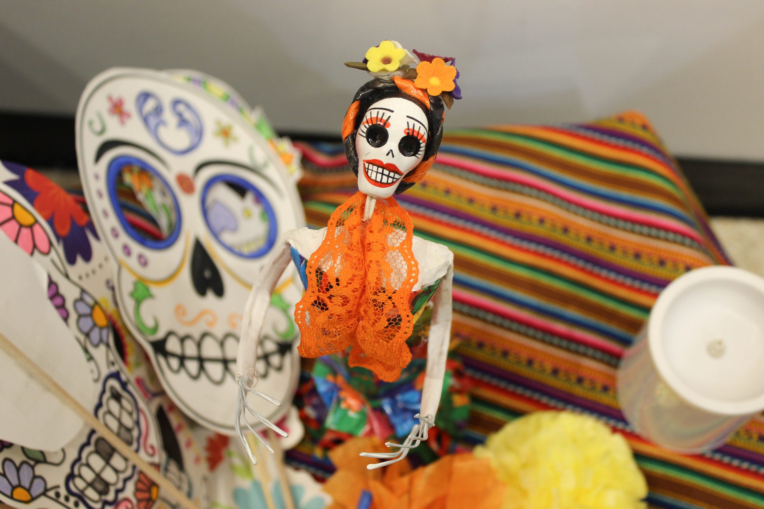 A colorful skeleton surrounded by paper skeleton masks and candles on top of an ofrenda.