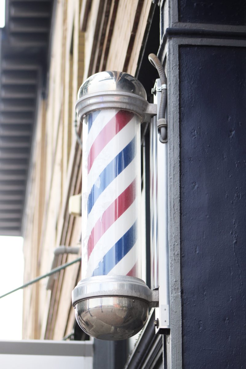 A barber pole attached to the outside of Moores Barbershop.