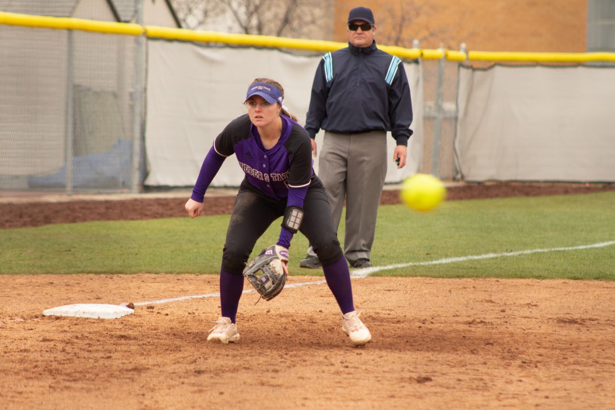Emily Ruhl and a referee watches the batter as the pitched ball flies past her. (Kennedy Robins/ The Signpost)