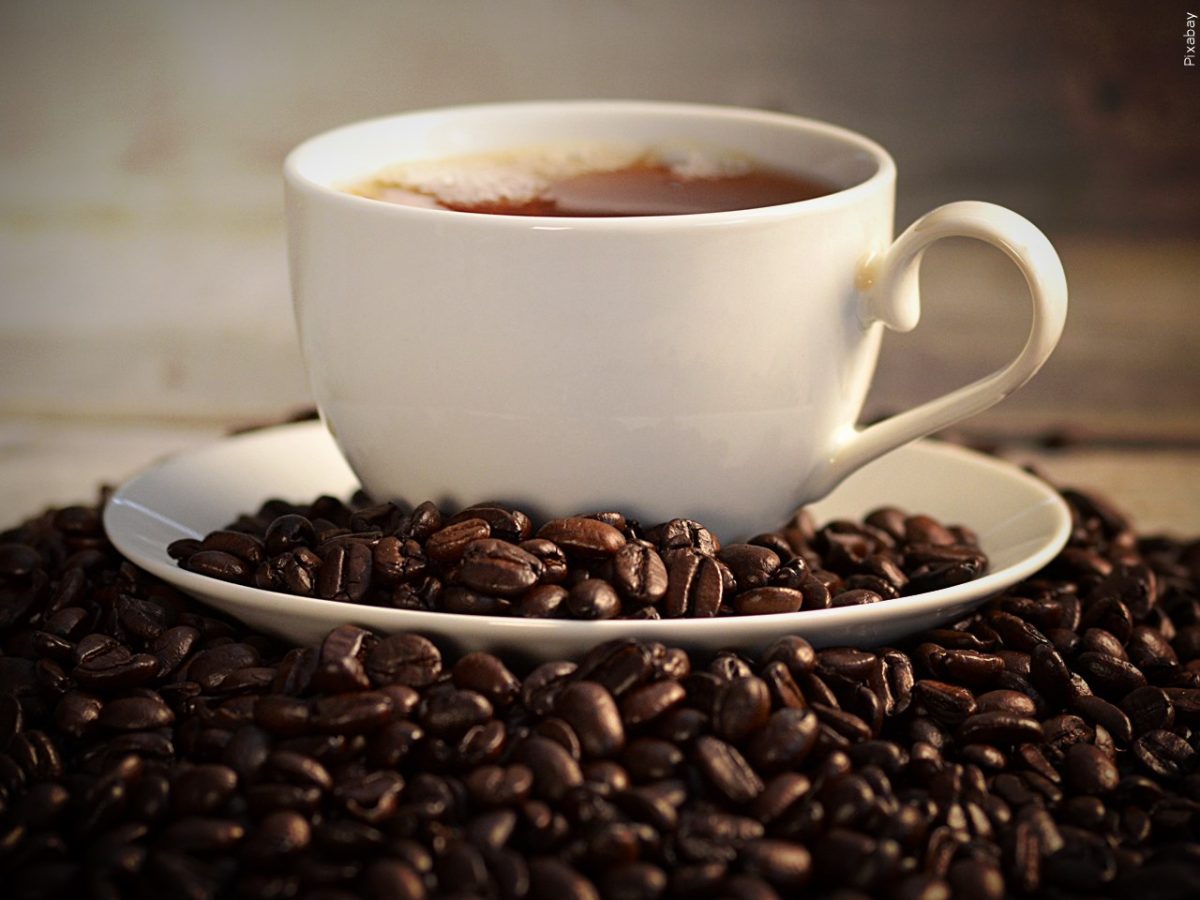 A photo of a latte in a coffee mug surrounded by fresh coffee beans.