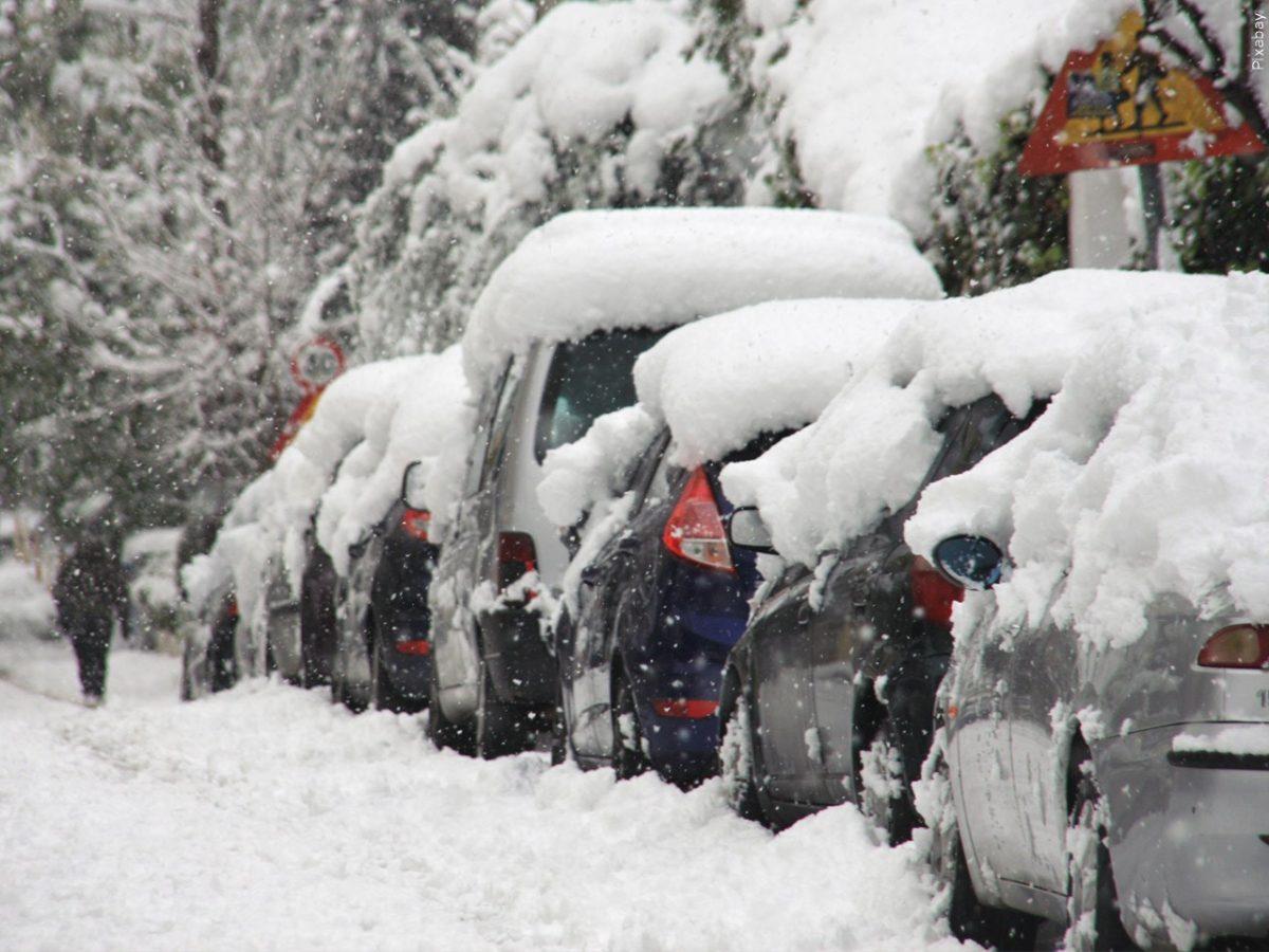 Cars line the street with large piles of snow on top.