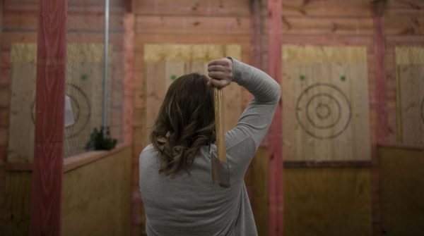 A woman prepares to aim the axe at the plywood target on the wall while axe throwing.