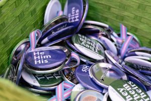 Pronoun pins set out for people to take at a pride event.// Pines de pronombres para que las personas agarren en el evento de orgullo.