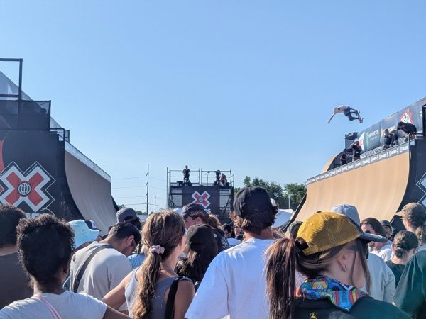 A crowd gathers to watch athletes take practice runs on the vert half pipe.// Una multitud se agrupa para observar a los atletas tomar rondas de practica en la media rampa vertical.
