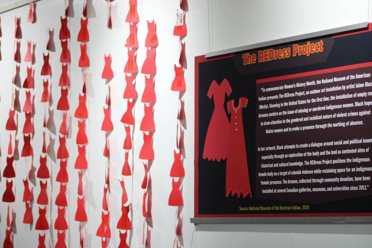 The REDress Project discloses the importance of the color red and empty dresses as symbolizing Missing and Murdered Indigenous Women, as it hangs up next to strung up cut-outs of red paper dresses in May of 2024. //The REDress Project discloses the importance of the color red and empty dresses as symbolizing Missing and Murdered Indigenous Women, as it hangs up next to strung up cut-outs of red paper dresses in May 2024. //El proyecto REDress revela la importancia del color rojo y los vestidos vacíos como símbolo de las mujeres indígenas desaparecidas y asesinadas, ya que se cuelga junto a recortes de vestidos de papel rojo en mayo de 2024
