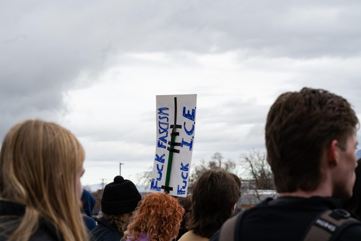 Weber State University students holding up a handmade poster that reads, "F*** Fascism, F*** I.C.E." in the crowd as they listen to fellow student speakers on Feb. 17, 2026. // Estudiantes de la Universidad Weber State sostienen un cartel hecho a mano en el que se lee "Que le den al fascismo, que le den al ICE" entre la multitud mientras escuchan a sus compañeros hablar el 17 de febrero de 2026.