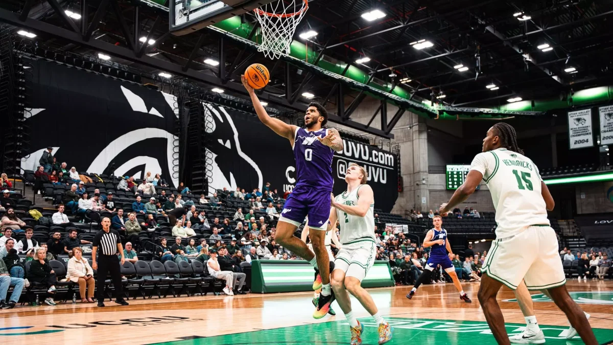 Weber State University men's basketball forward Edwin Suarez Jr. (#0) jumps to make a dunk on Utah Valley University players. // El alero del equipo masculino de baloncesto de la Universidad Estatal de Weber, Edwin Suárez Jr. (n.º 0), salta para hacer un mate sobre los jugadores de la Universidad de Utah Valley.