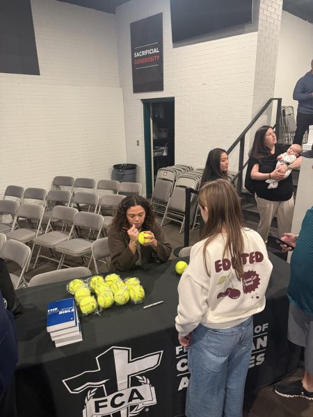 Alyssa Brito signs a softball at a table at Redemption Church April 9. // Alyssa Brito firma una pelota de sóftbol en una mesa de la iglesia Redemption el 9 de abril.